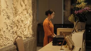 A person standing at a counter with a laptop, a vase of flowers, and a wall with intricate carvings.