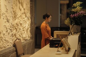 A person standing at a counter with a laptop, a vase of flowers, and a wall with intricate carvings.