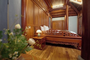 A traditional wooden bedroom with a four-poster bed, a nightstand, and a bedside table with a lamp.