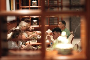 Un grupo de personas cenando en una mesa con vista a una estantería al fondo.