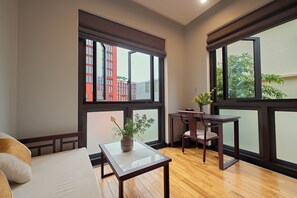 A room with a sofa, a small table, and a chair. There are large windows with a view of buildings and trees. - Thong Dong Quan Boutique Hotel Hue (Thuan Hoa)