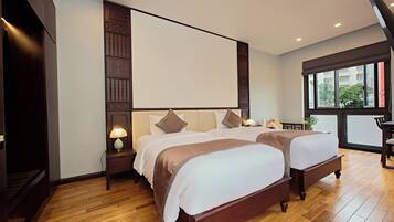 A hotel room with two beds, wooden flooring, a large window, and a view of the outside.