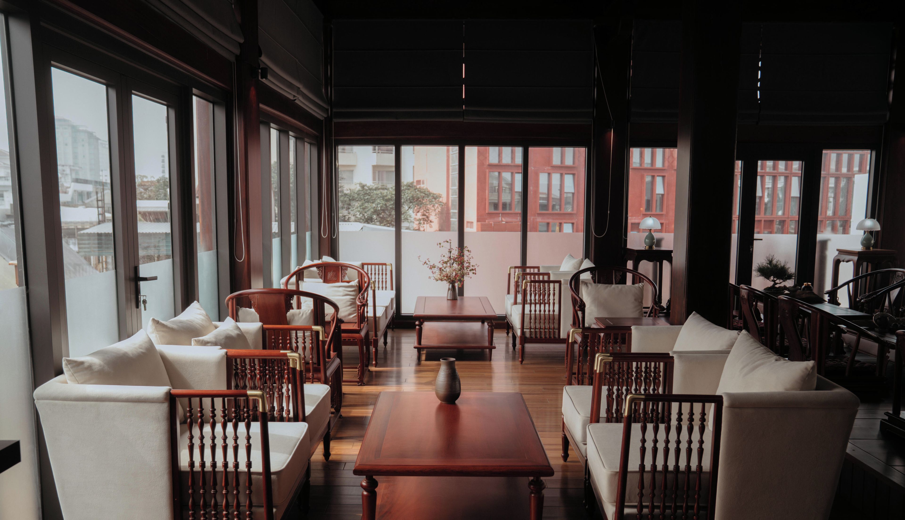 Una habitación amplia con ventanas grandes, muebles de madera y vistas a edificios.