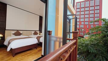 A hotel room with a large bed, wooden floor, and a view of a red building through a glass door.