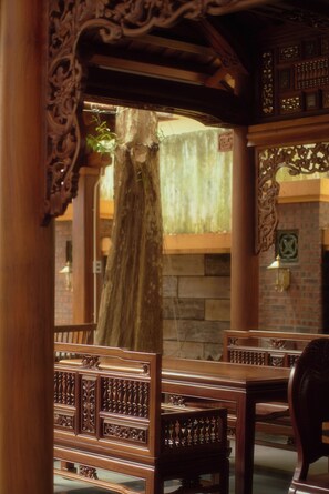 A traditional wooden interior with ornate carvings, a stone wall, and a large tree trunk. - Thong Dong Quan Boutique Hotel Hue (Thuan Hoa)
