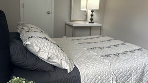 A bedroom with a bed, a bedside table with a lamp, a potted plant, and a door.
