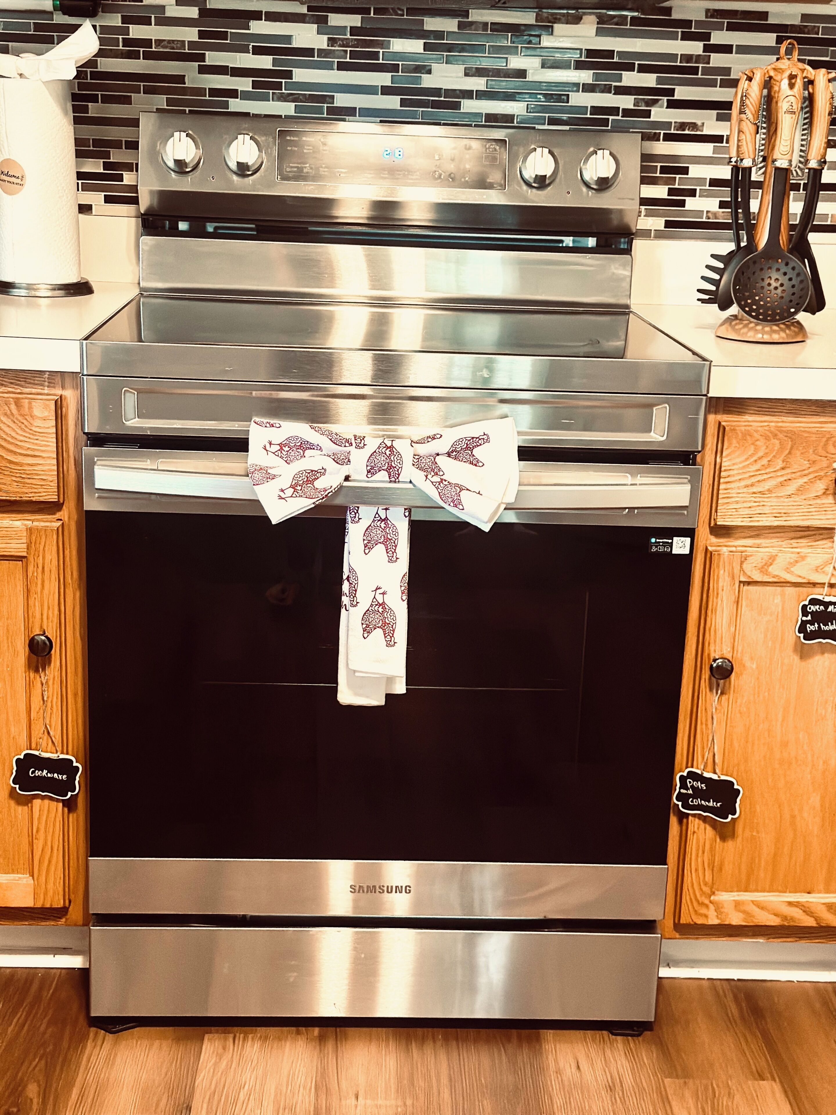 Forno in acciaio inox con pannello di controllo digitale, schienale della cucina rivestito con mosaico e pensili con etichette.
