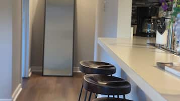 Une cuisine avec un plan de travail blanc, un réfrigérateur et trois tabourets de bar noirs.