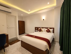 A hotel room with a large bed, a wardrobe, a desk, and a green curtain.