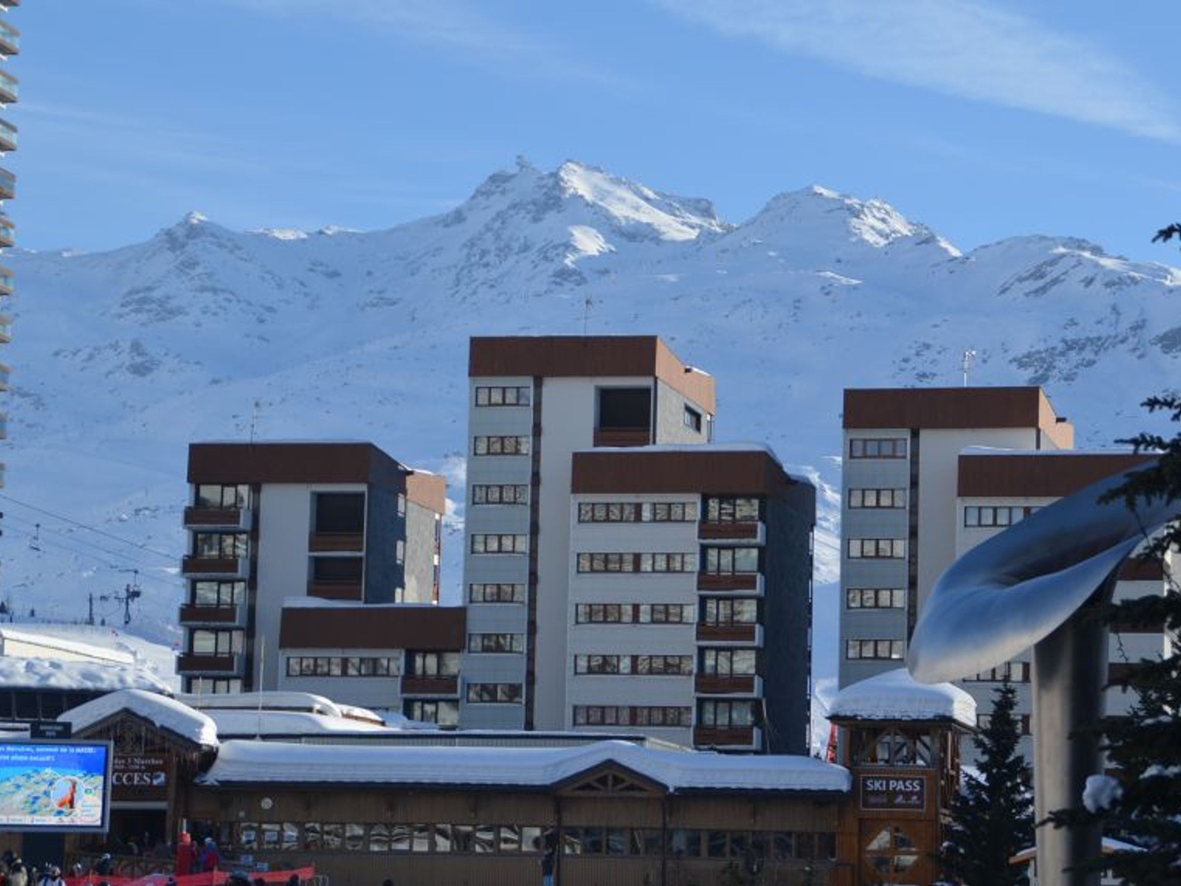 Un hôtel à plusieurs étages, avec un panneau indiquant les tarifs des forfaits de ski, et des montagnes enneigées en arrière-plan.