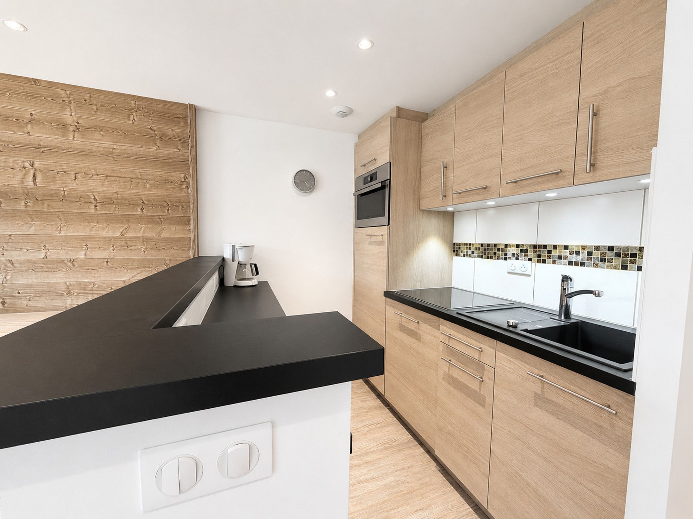 Een moderne keuken met houten kastjes, een zwart aanrecht en een inbouwoven.
