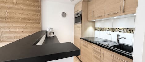 Cozinha moderna com armários de madeira, bancada preta e forno embutido.