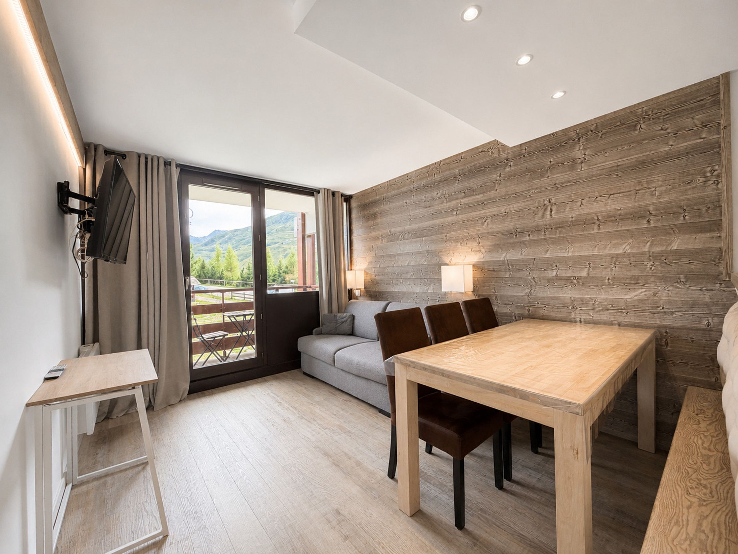 Een moderne kamer met een houten eettafel, een bank en een balkon met uitzicht op bergen.