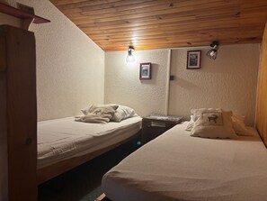 A room with two beds, wooden ceiling, textured walls, and a small table with a lamp. - Duplex with valley view - 10 guests (La Plagne Montchavin Les Coches)