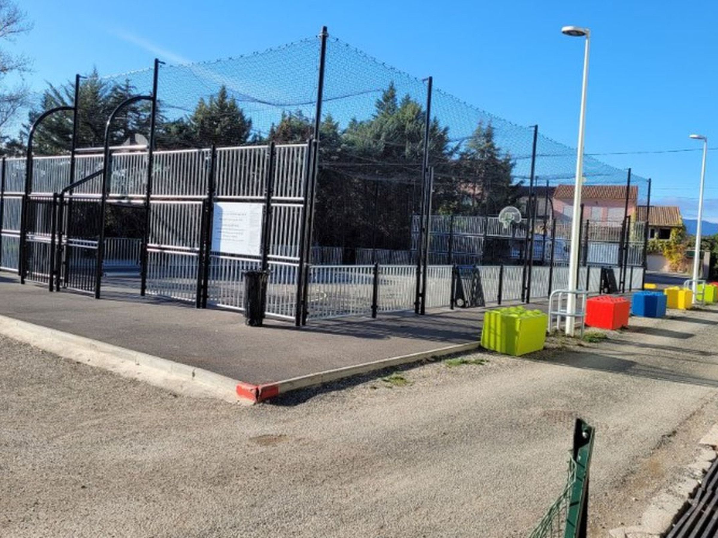 Uma área cercada com quadra de basquete, lixeira e caixas organizadoras coloridas.