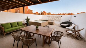 Eine Terrasse im Freien mit einem Holztisch, Korbstühlen, einem grünen Sofa und einem schwarzen Liegestuhl.