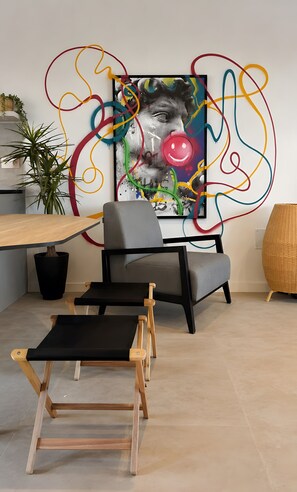 Un interior moderno con una mesa de madera, una silla de oficina gris, un banco de ejercicios negro y un cuadro abstracto de colores en la pared.