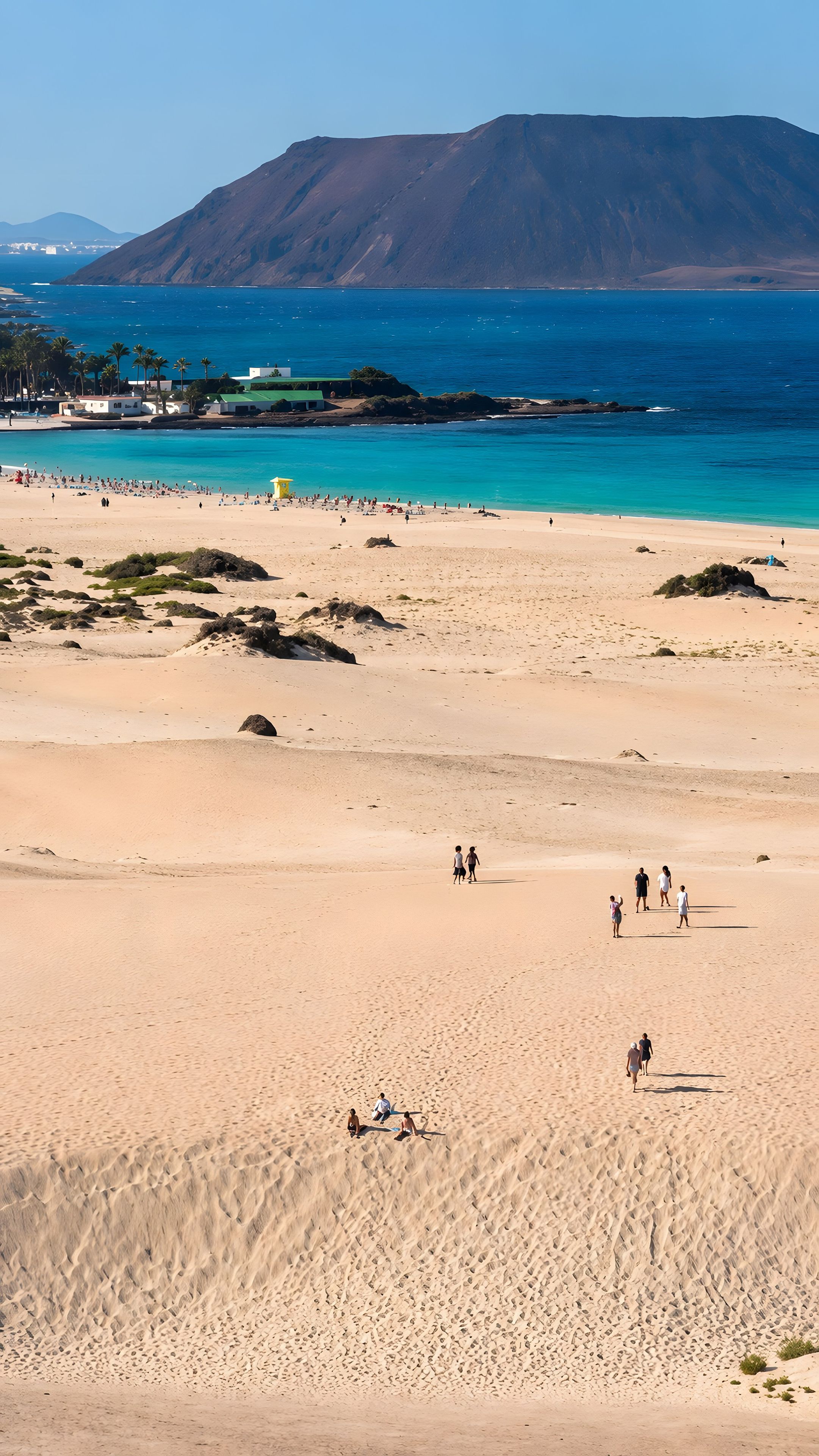 Ein Strand mit Menschen, die spazieren gehen und sitzen, ein klarer Himmel und ein Berg im Hintergrund.