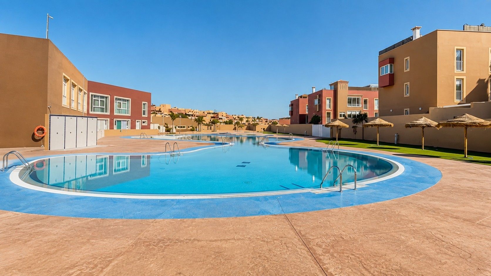 Une piscine dont le bord est bleu, entourée de bâtiments présentant un style architectural uniforme.