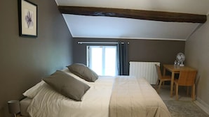 A bedroom with a bed, a bedside table, a chair, a desk with a fan, and a window with curtains. - Comfortable Family Room with Breakfast at the Farm (Grandrupt-de-Bains)