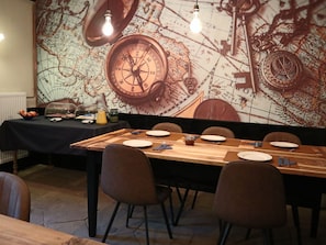A dining area with a long table set for four, a vintage map mural on the wall, and a vintage compass.