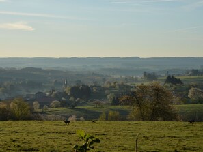 A rural landscape with rolling hills, a church spire, and a deer in a field.