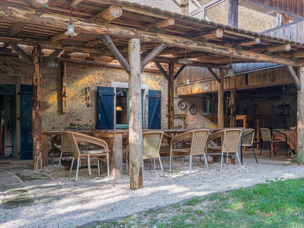 An outdoor wooden structure with a table and chairs, a rustic interior with a wooden ceiling, and a stone wall.