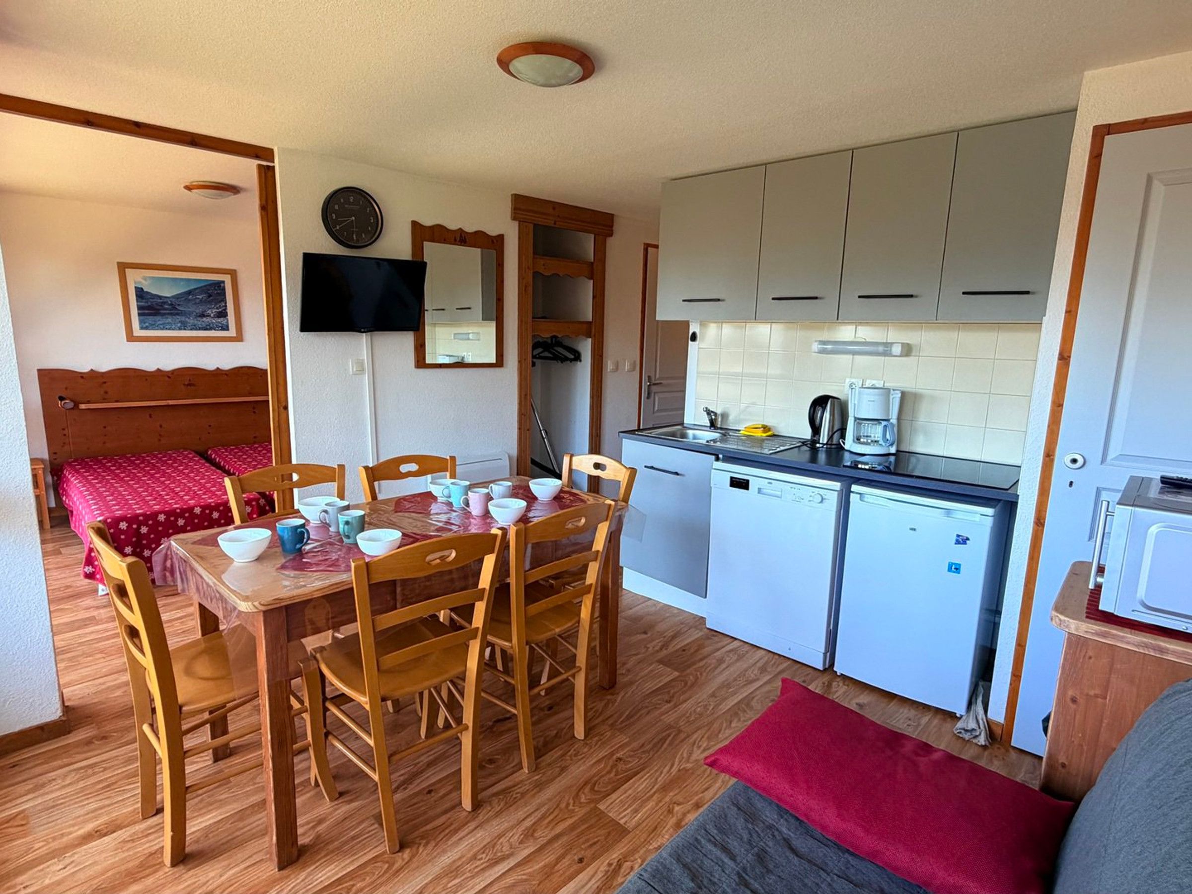 A compact kitchen with a dining area, wooden furniture, and a television on the wall.