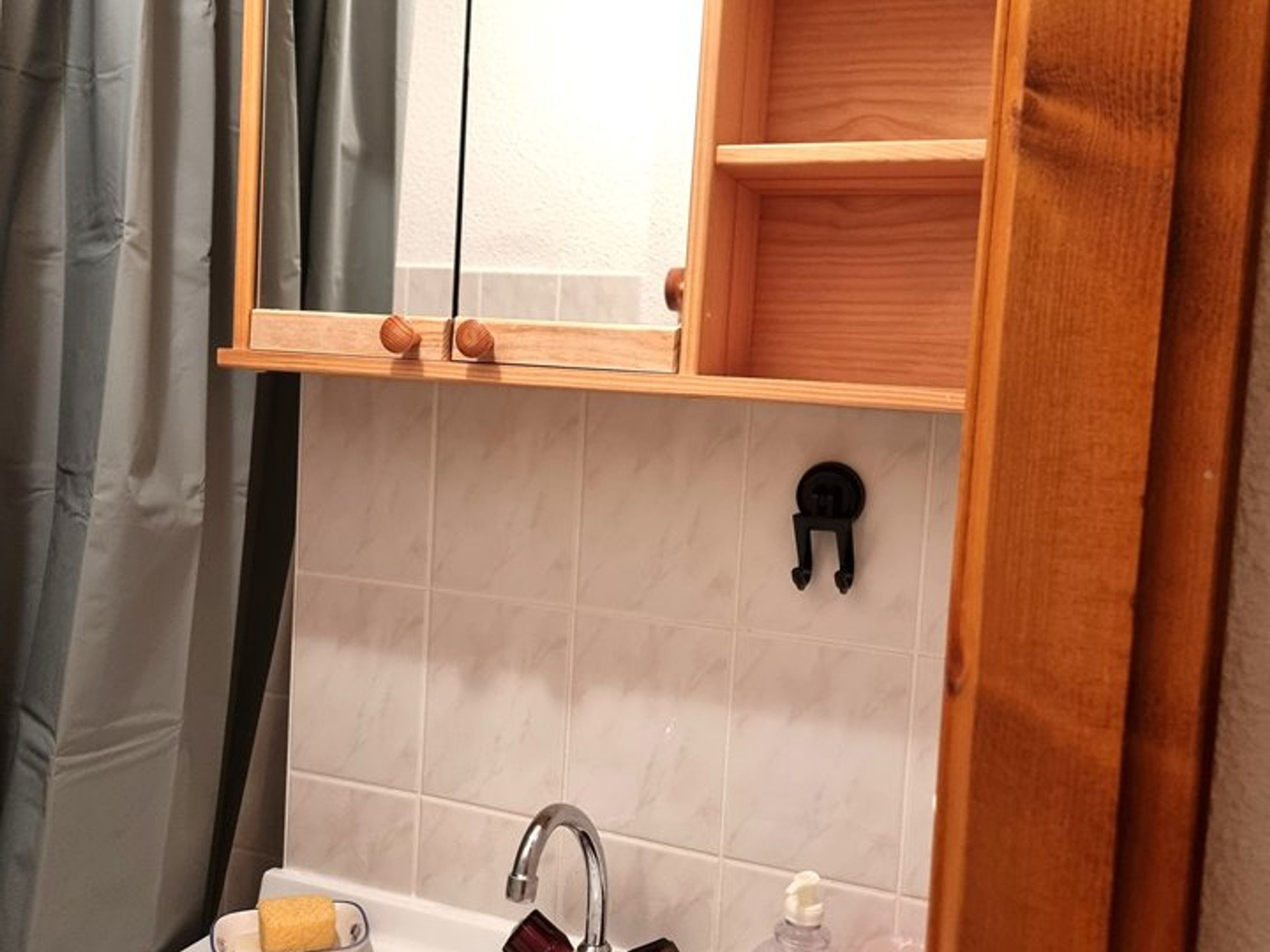 Een badkamer met een houten kastje boven de wasbak, een handdoekhouder en een spiegel.