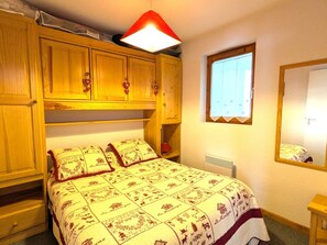 A bedroom with a bed, wooden wardrobe, a window, and a mirror. - Cozy apartment at the foot of the slopes - 2 guests (Saint-Jean-d'Aulps)