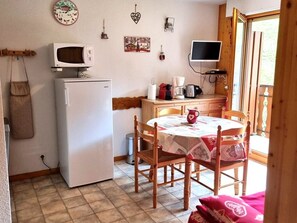 Een compacte keuken met een koelkast, magnetron en een kleine televisie. Er is een eettafel met stoelen en een raam met uitzicht.
