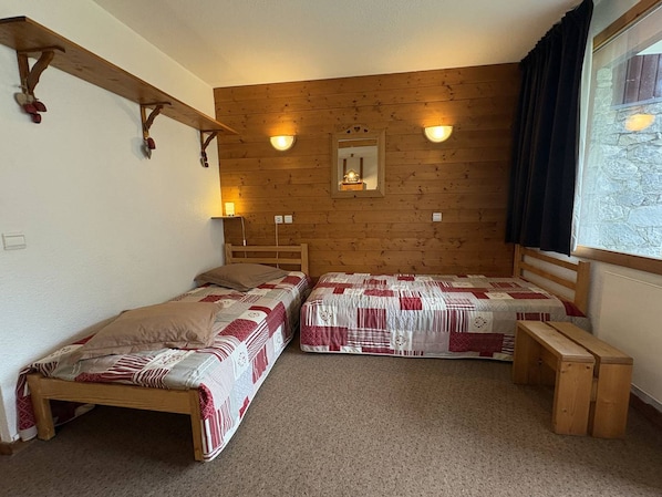 A room with two wooden beds, a mirror, and a window with curtains.