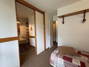 A bedroom with a bed, a wooden door, a small table with chairs, and a hallway. - Ground floor apartment - pets welcome - 4 guests (Valmorel)