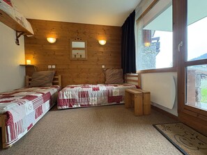 A room with two single beds, a wooden headboard, a small wooden table, and a window with curtains. - Ground floor apartment - pets welcome - 4 guests (Valmorel)