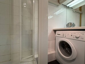 A laundry area with a washing machine and a glass shower enclosure.