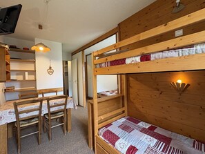A bunk bed with a quilt, a wooden table with chairs, and a television. - Ground floor apartment - pets welcome - 4 guests (Valmorel)