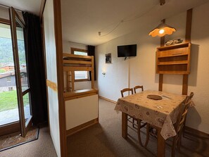 A room with a bunk bed, a dining table with chairs, a television mounted on the wall, and a window with curtains. - Ground floor apartment - pets welcome - 4 guests (Valmorel)