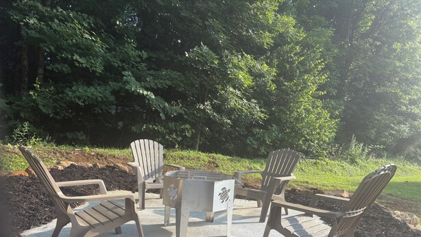 Espace extérieur aménagé avec des chaises Adirondack et une table centrale, le tout entouré d’arbres.