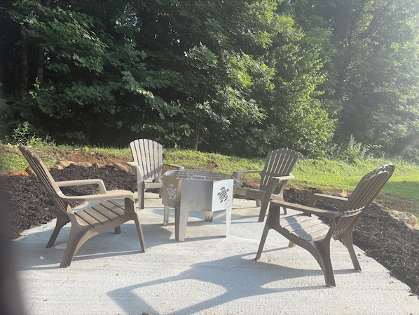 Espace extérieur aménagé avec des chaises Adirondack et une table centrale, le tout entouré d’arbres.