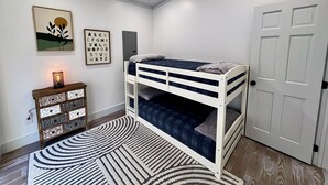 Une chambre avec un lit superposé, une porte blanche, une petite commode avec des tiroirs, un tapis et des décorations murales.