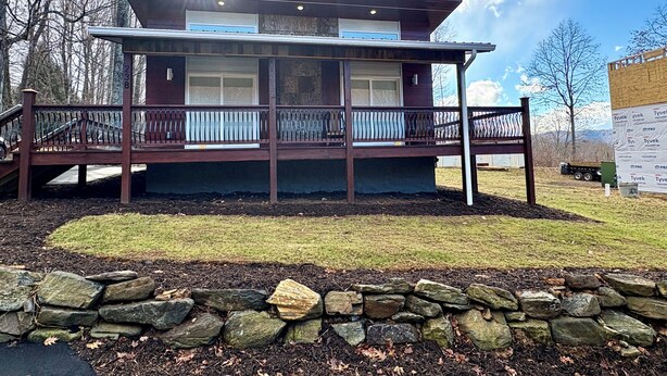 Une cabane à deux étages dotée d’un balcon, entourée d’un mur de pierre et d’une zone herbeuse.