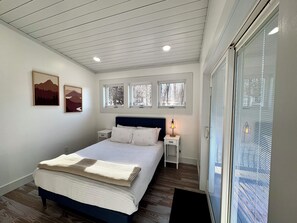 Ein Schlafzimmer mit einem Bett, Nachttischen, einer Lampe und Fenstern.