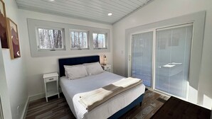 Une chambre à coucher avec un lit, des tables de chevet, une fenêtre et une porte-fenêtre coulissante.