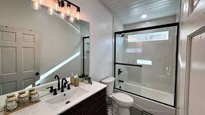 Une salle de bain moderne avec un grand miroir, un lavabo blanc, des toilettes et une douche à parois de verre.