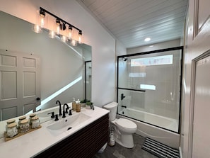 Un bagno moderno con uno specchio grande, un lavandino bianco, un WC e una cabina doccia in vetro.