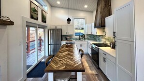 Une cuisine moderne avec une longue table en bois, des armoires blanches et un grand réfrigérateur.