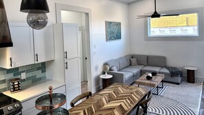 Une cuisine moderne avec des meubles blancs, une table à manger au motif en chevrons et une grande fenêtre donnant sur un immeuble.