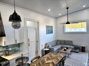 Une cuisine moderne avec des meubles blancs, une table à manger au motif en chevrons et une grande fenêtre donnant sur un immeuble.