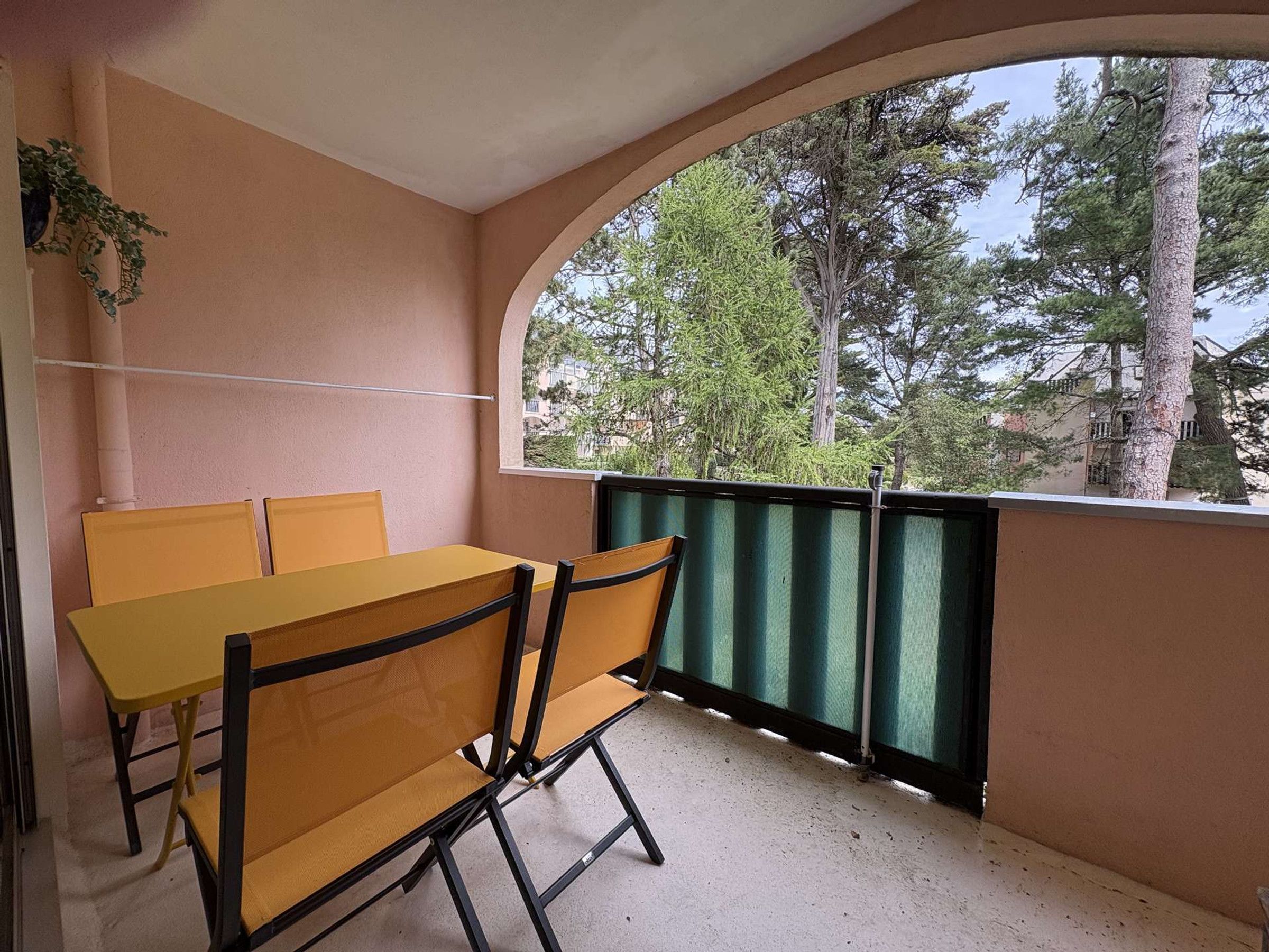 A balcony with a table and chairs, a view of trees, and a building in the background.