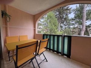 Een balkon met een tafel en stoelen, uitzicht op bomen en een gebouw op de achtergrond.